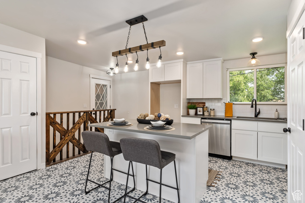 Kitchen featuring white cabinets, a kitchen breakfast bar, dishwasher, pendant lighting, and a center island