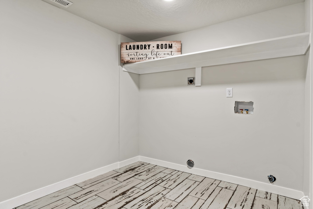 Laundry area with a textured ceiling, washer hookup, light wood-type flooring, and electric dryer hookup