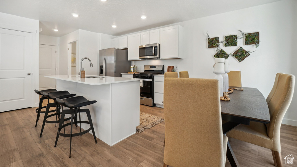 Kitchen featuring light hardwood / wood-style flooring, sink, stainless steel appliances, a breakfast bar, and a kitchen island with sink