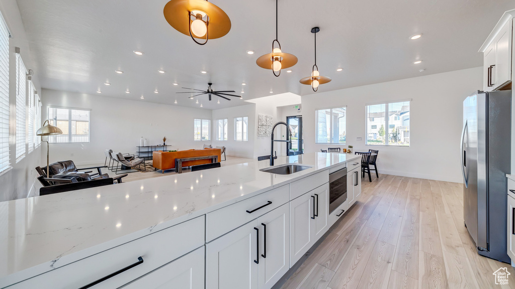 Kitchen featuring sink, white cabinetry, light hardwood / wood-style floors, pendant lighting, and stainless steel refrigerator with ice dispenser