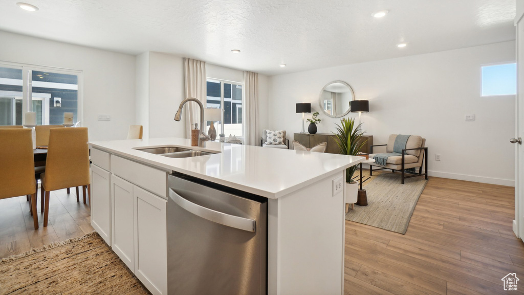 Kitchen with sink, dishwasher, white cabinetry, light hardwood / wood-style floors, and a center island with sink