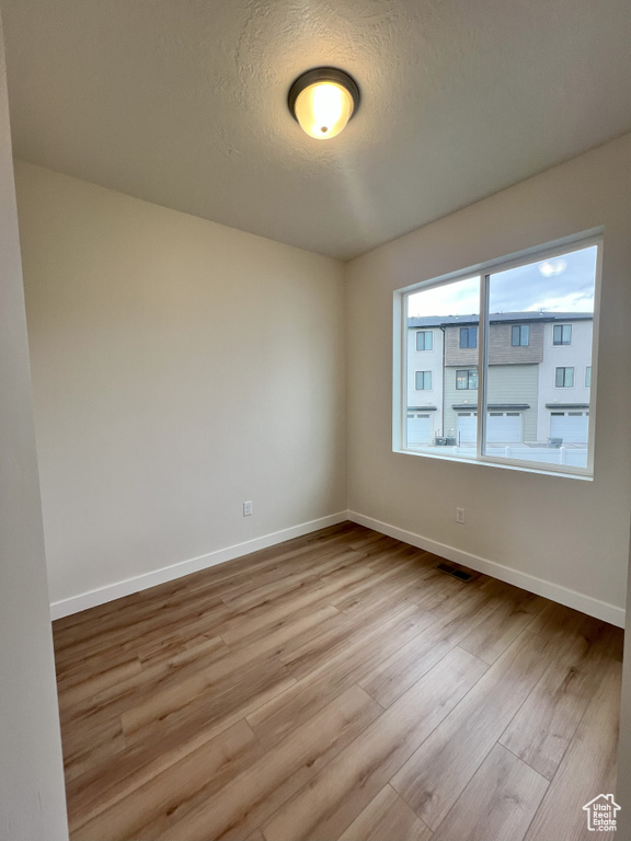 Empty room with a textured ceiling and light hardwood / wood-style flooring