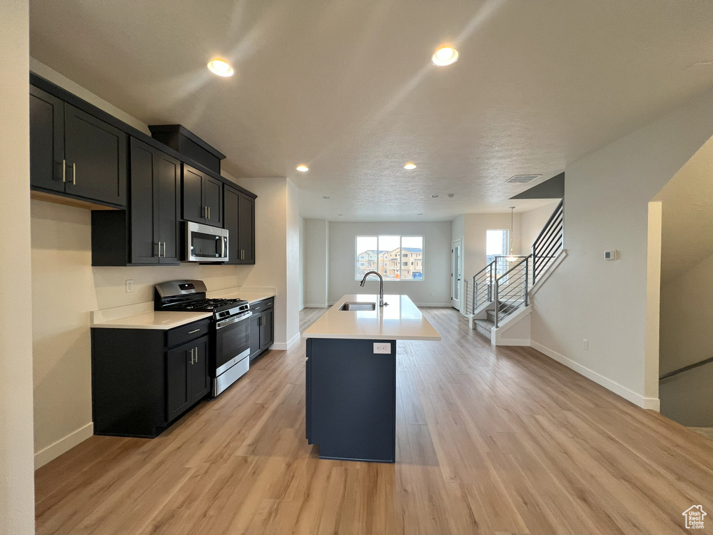 Kitchen featuring sink, an island with sink, a textured ceiling, light hardwood / wood-style floors, and stainless steel appliances