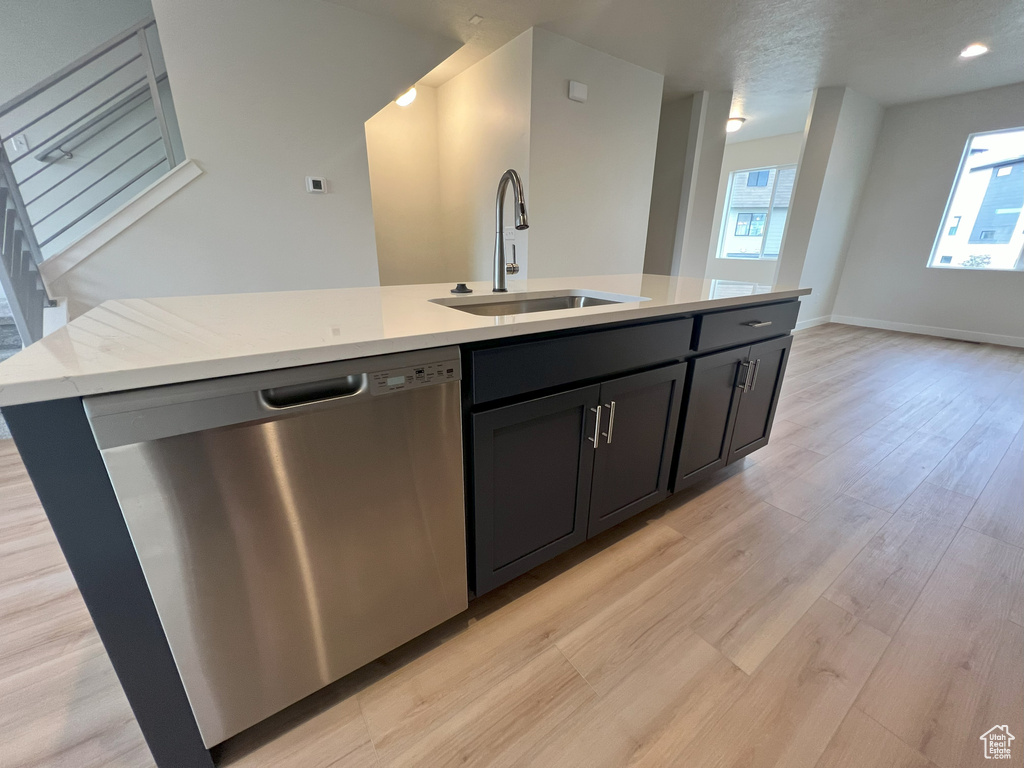 Kitchen with light stone countertops, sink, dishwasher, light wood-type flooring, and a center island with sink