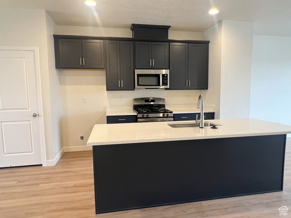 Kitchen with a kitchen island with sink, stainless steel appliances, sink, and light wood-type flooring