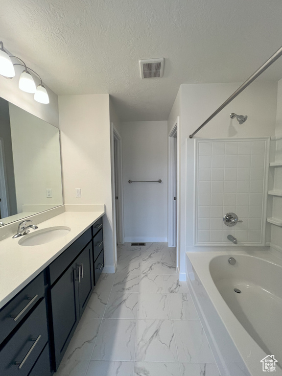 Bathroom with tiled shower / bath, vanity, and a textured ceiling