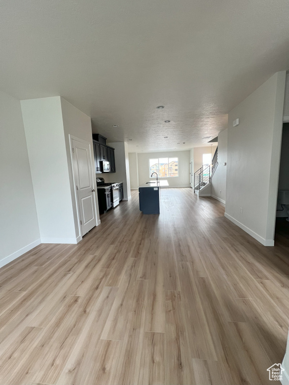 Unfurnished living room with sink, a textured ceiling, and light wood-type flooring