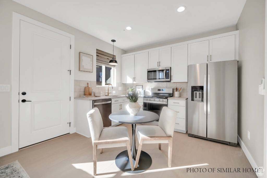 Kitchen featuring tasteful backsplash, decorative light fixtures, white cabinetry, stainless steel appliances, and light wood-type flooring