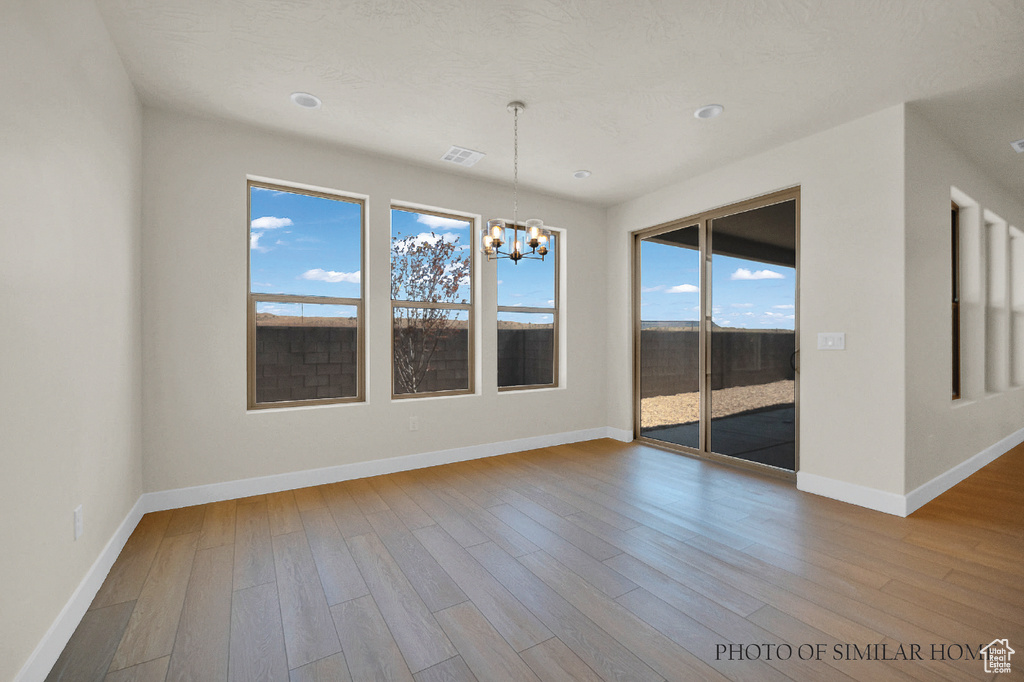 Spare room with an inviting chandelier, hardwood / wood-style floors, and a healthy amount of sunlight