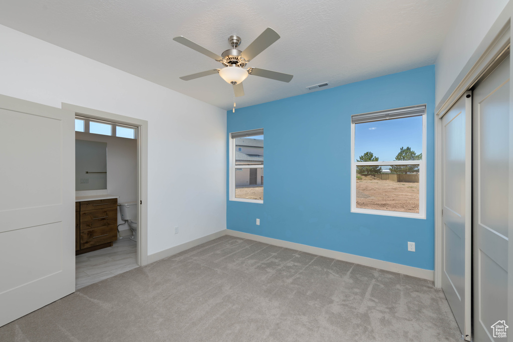 Unfurnished bedroom with ensuite bath, light carpet, and ceiling fan