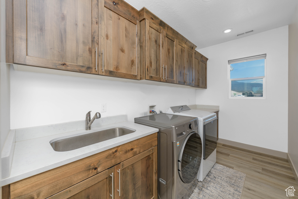 Washroom featuring independent washer and dryer, cabinets, sink, and light wood-type flooring