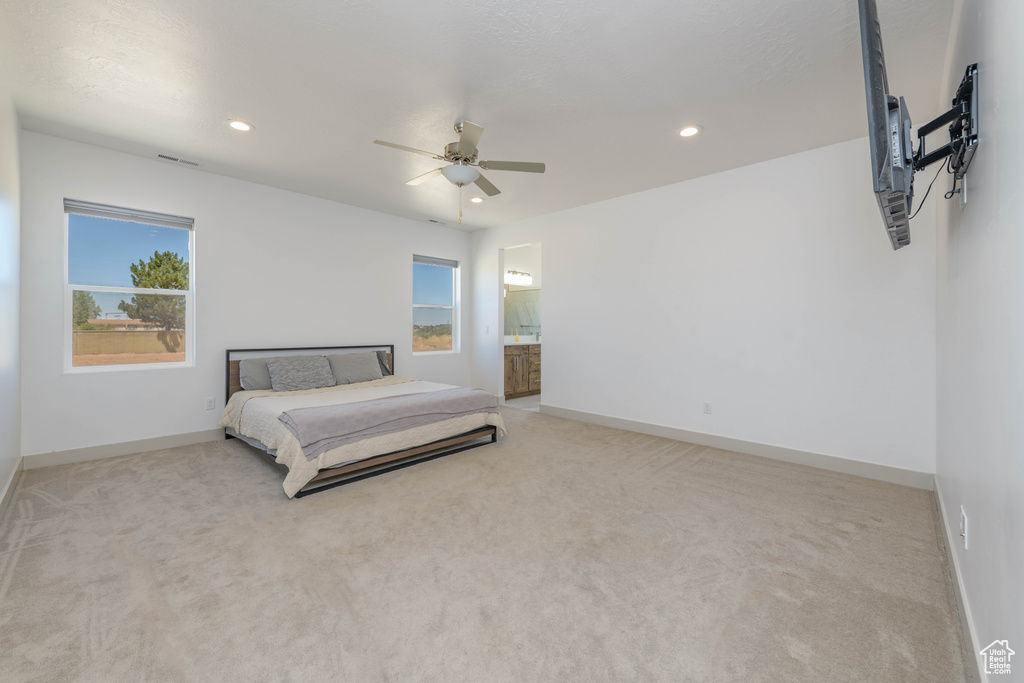 Bedroom featuring ensuite bath, light carpet, and ceiling fan