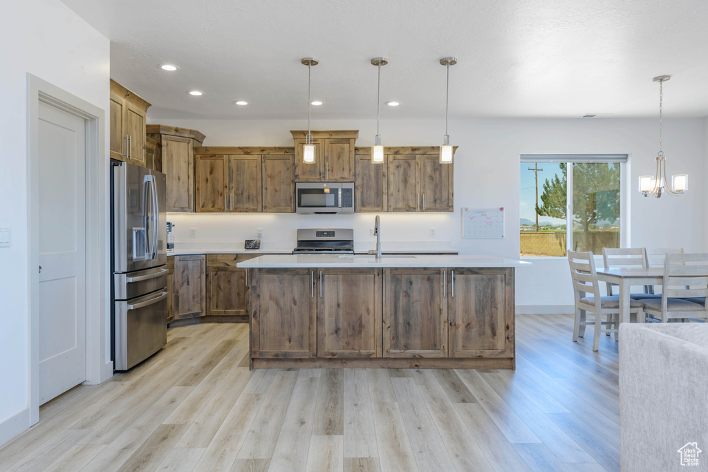 Kitchen featuring light hardwood / wood-style floors, appliances with stainless steel finishes, and hanging light fixtures