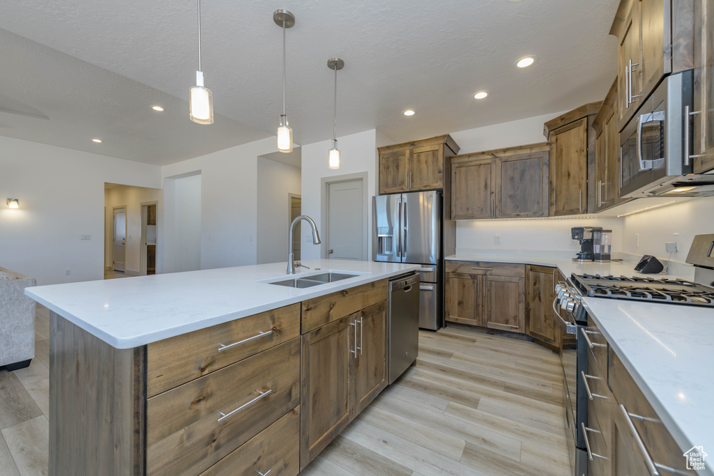 Kitchen featuring a kitchen island with sink, hanging light fixtures, stainless steel appliances, sink, and light hardwood / wood-style floors