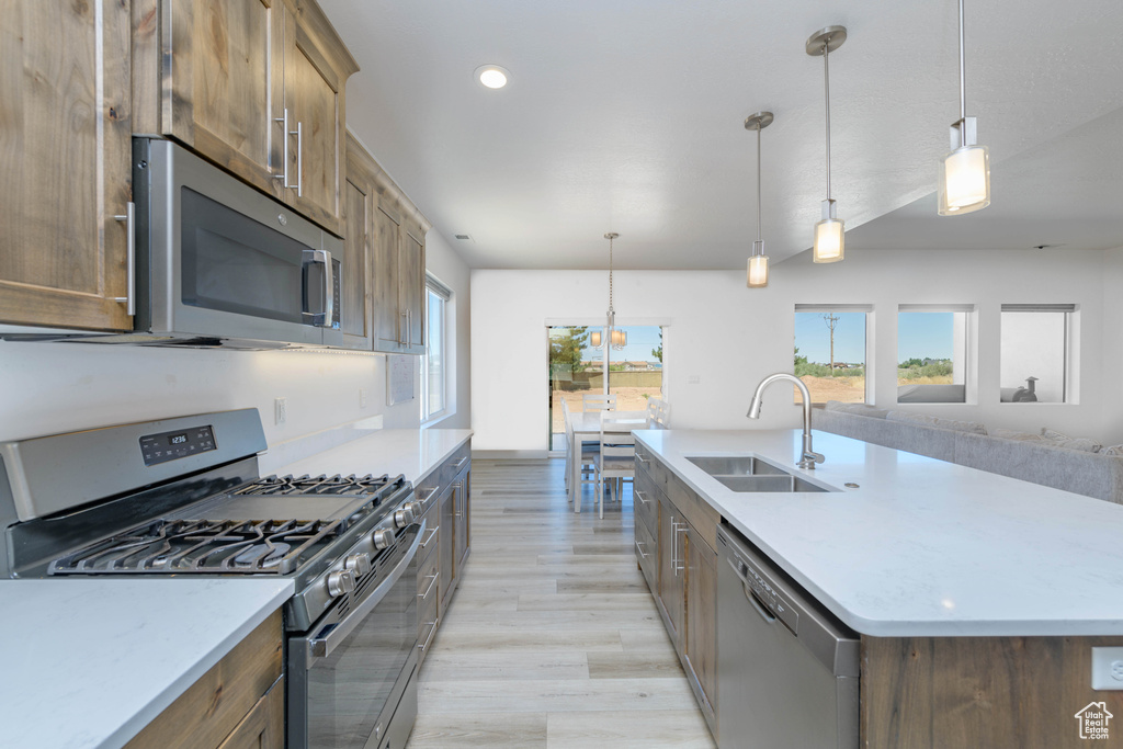 Kitchen with appliances with stainless steel finishes, hanging light fixtures, light wood-type flooring, and an island with sink