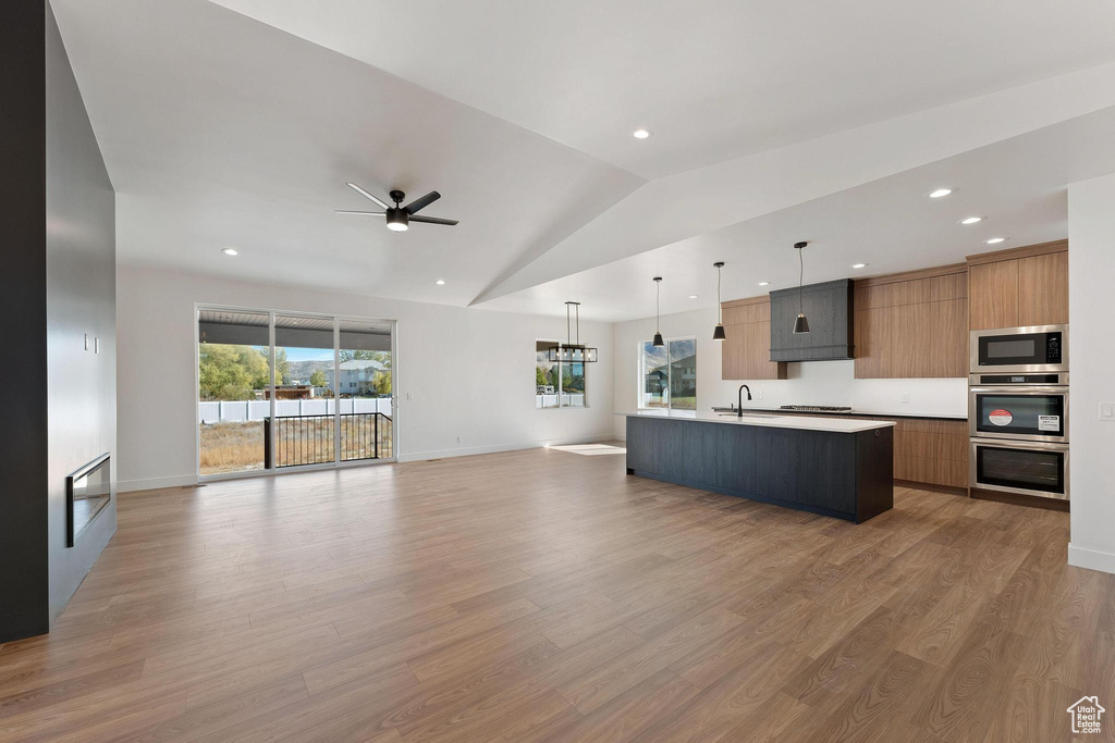 Kitchen featuring appliances with stainless steel finishes, lofted ceiling, an island with sink, and hardwood / wood-style flooring