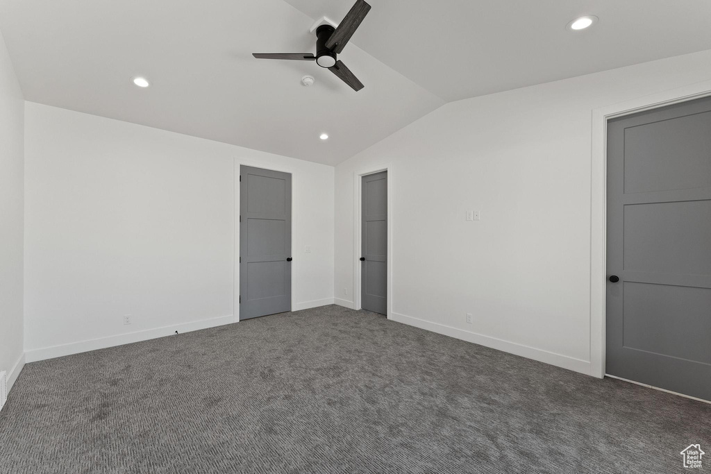 Unfurnished bedroom with dark colored carpet, vaulted ceiling, and ceiling fan