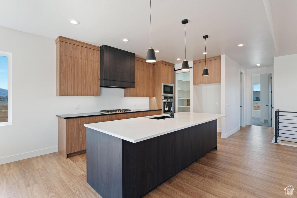 Kitchen featuring sink, a spacious island, hanging light fixtures, light hardwood / wood-style floors, and custom range hood