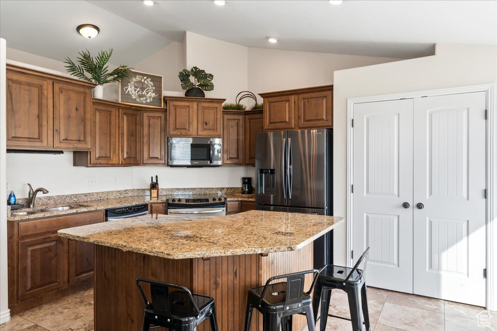 Kitchen featuring a center island, stainless steel appliances, vaulted ceiling, and a kitchen bar