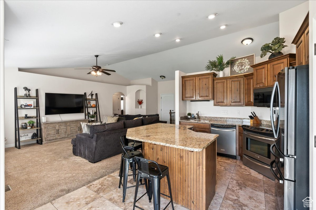 Kitchen with appliances with stainless steel finishes, a breakfast bar, vaulted ceiling, a center island, and light colored carpet