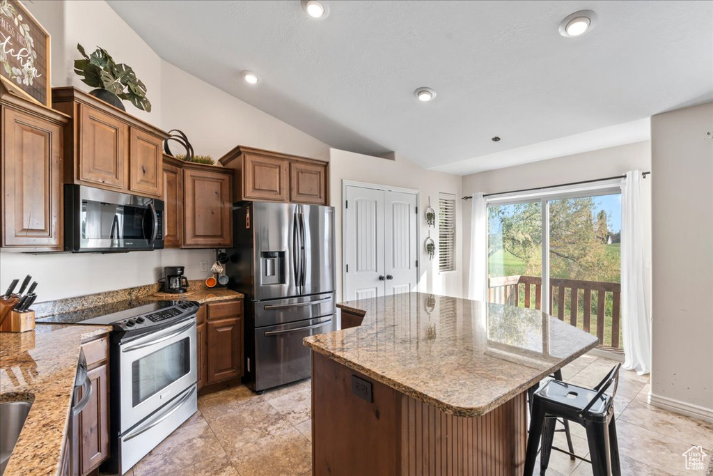 Kitchen with light stone counters, appliances with stainless steel finishes, a breakfast bar, vaulted ceiling, and a center island