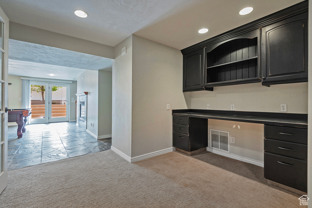 Kitchen featuring built in desk, french doors, a textured ceiling, and light colored carpet