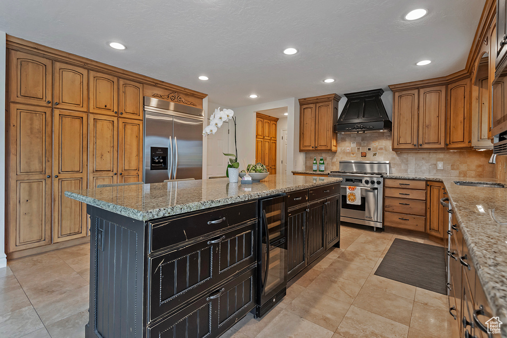 Kitchen featuring custom exhaust hood, wine cooler, a kitchen island, light stone countertops, and premium appliances