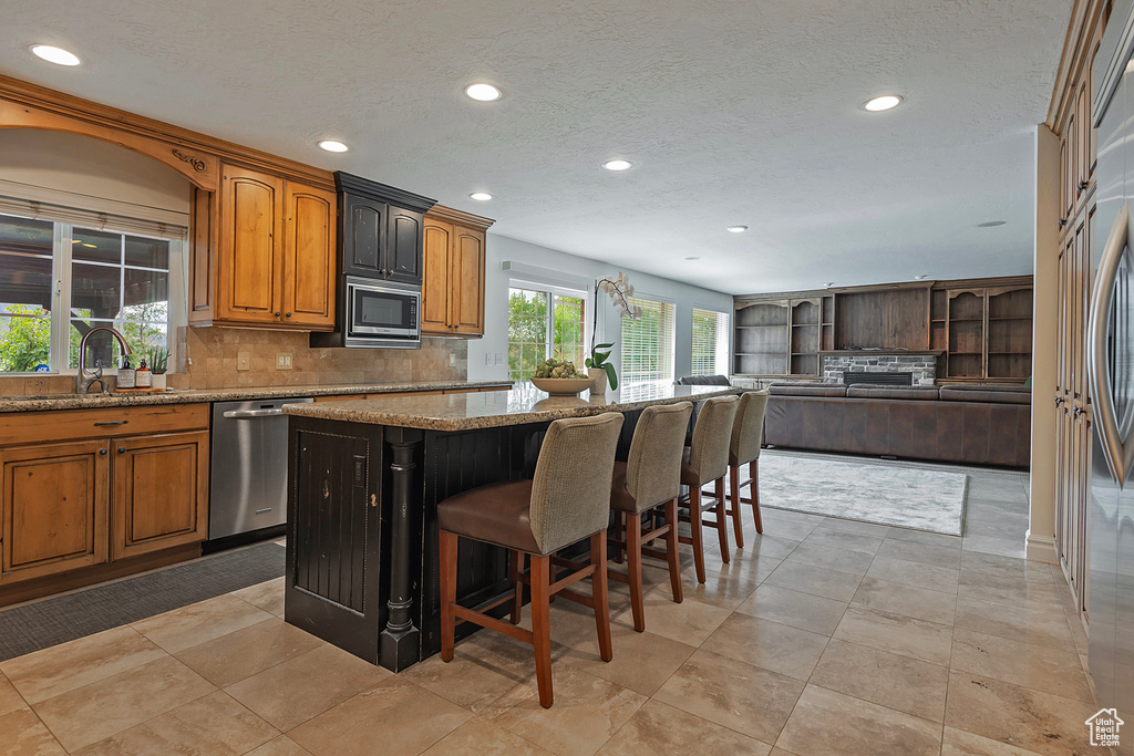 Kitchen featuring light stone counters, a kitchen breakfast bar, stainless steel appliances, sink, and a center island