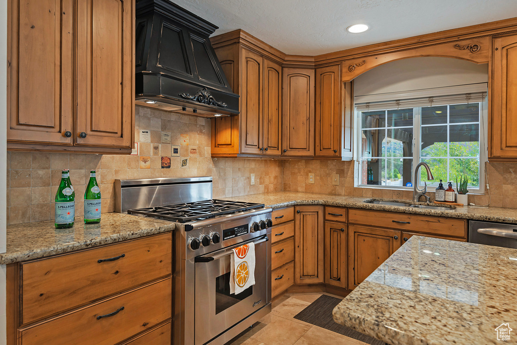 Kitchen featuring sink, backsplash, custom exhaust hood, high end stove, and light stone counters