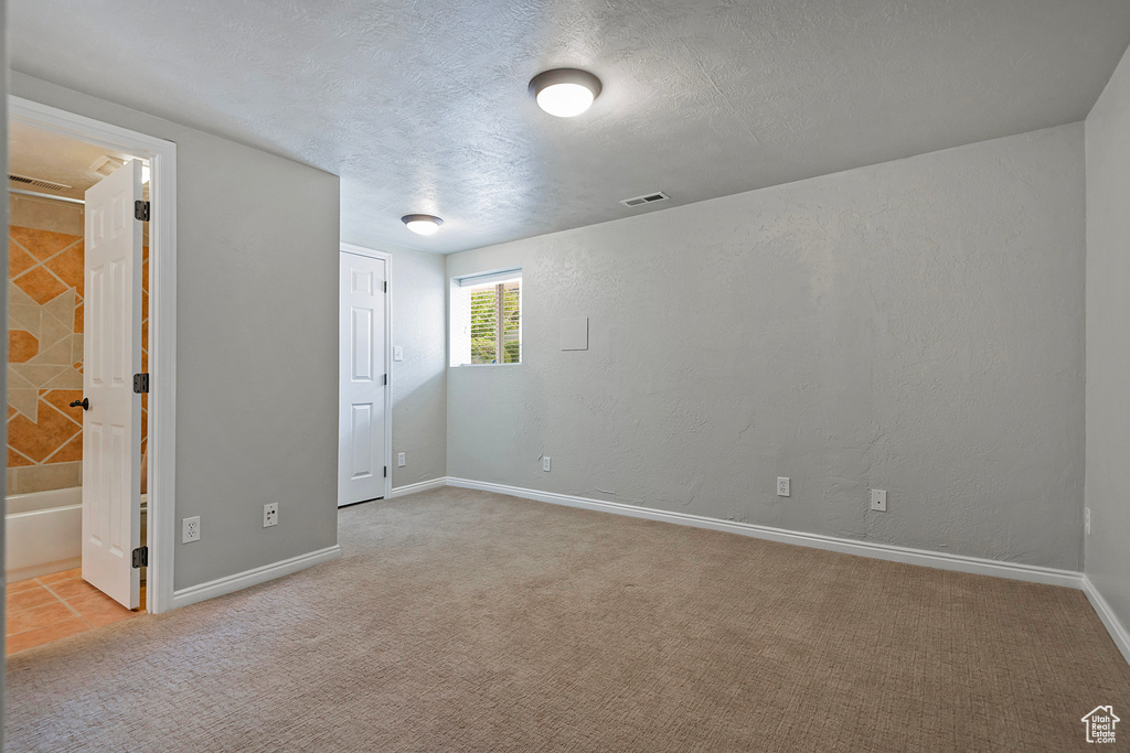 Unfurnished bedroom with a textured ceiling, ensuite bathroom, and light colored carpet