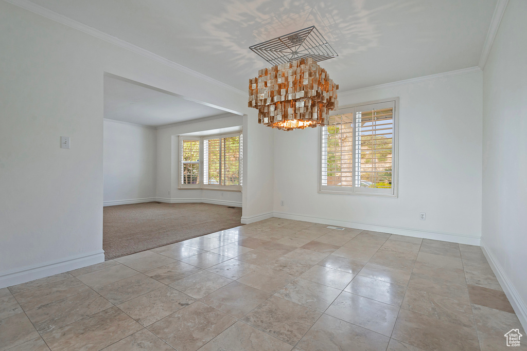 Unfurnished room featuring a notable chandelier, crown molding, and light carpet