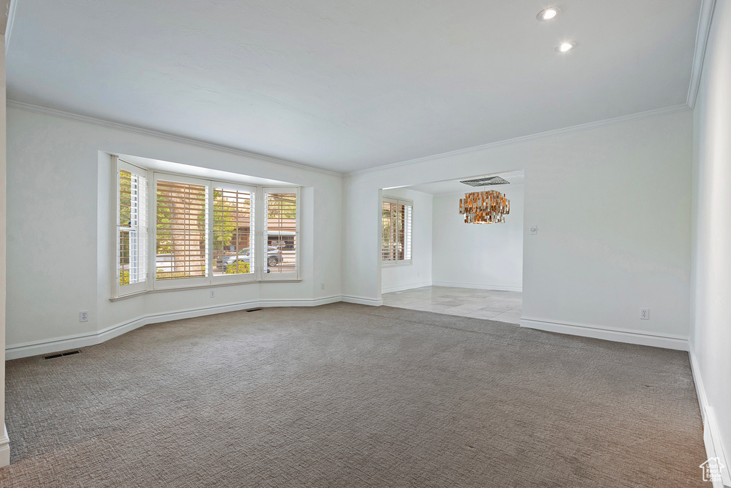 Carpeted empty room with crown molding and a chandelier