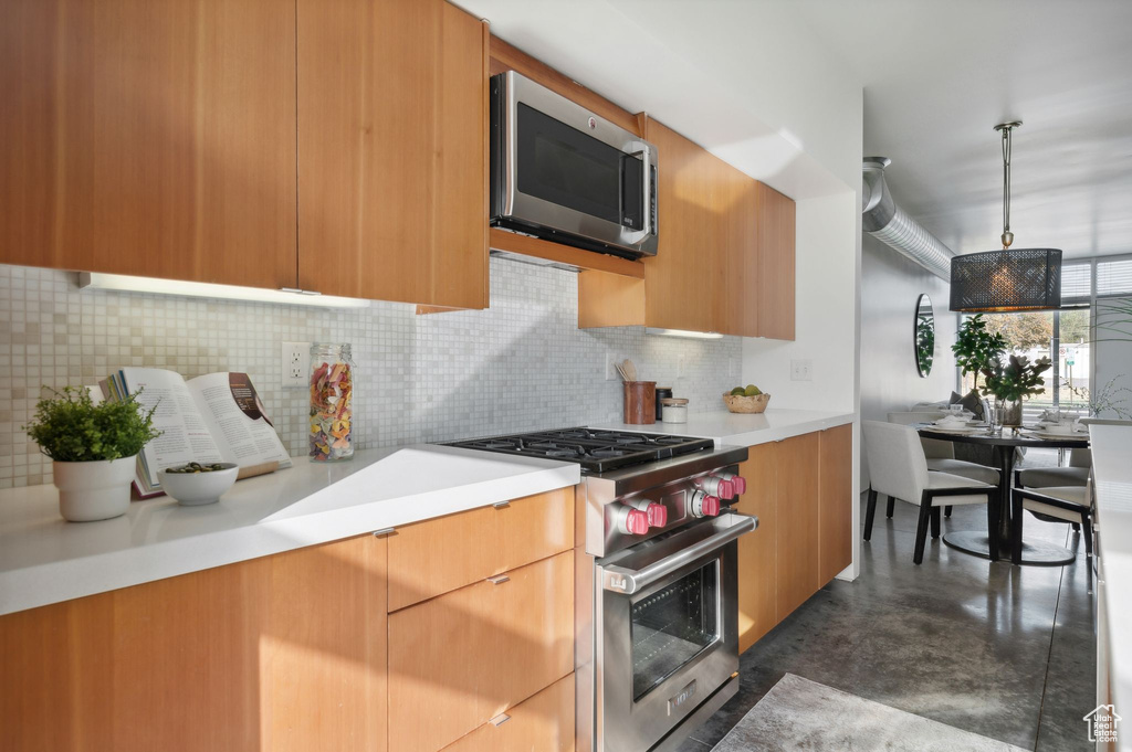 Kitchen featuring appliances with stainless steel finishes, decorative backsplash, and hanging light fixtures