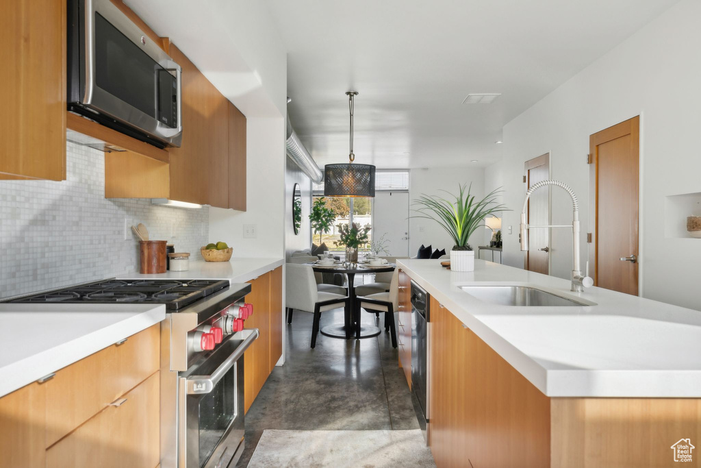 Kitchen featuring stainless steel appliances, backsplash, a center island with sink, sink, and pendant lighting