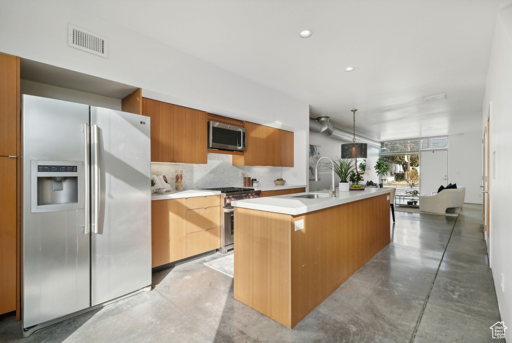 Kitchen with sink, backsplash, hanging light fixtures, stainless steel appliances, and a center island with sink