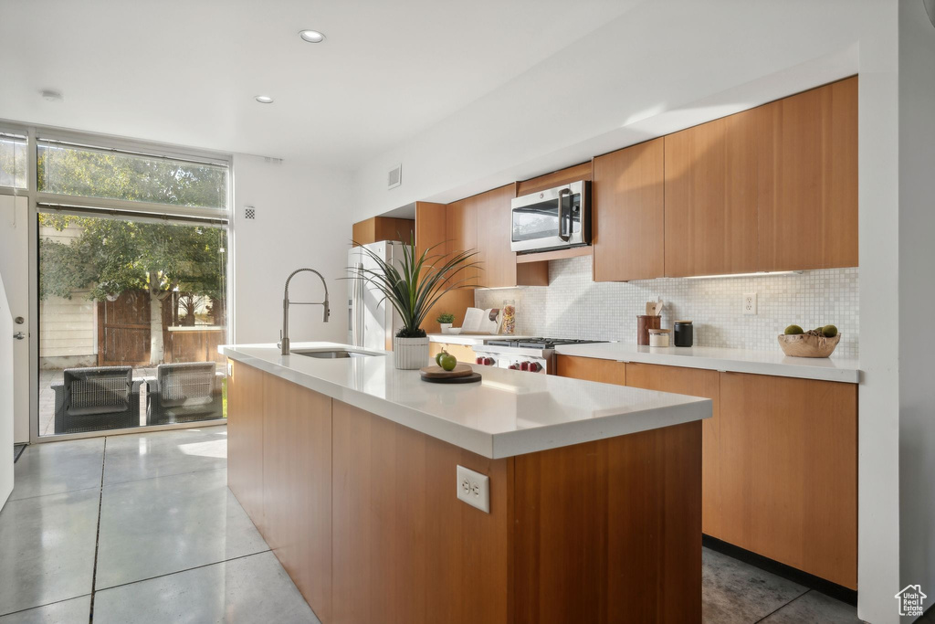 Kitchen featuring backsplash, appliances with stainless steel finishes, sink, and a kitchen island with sink