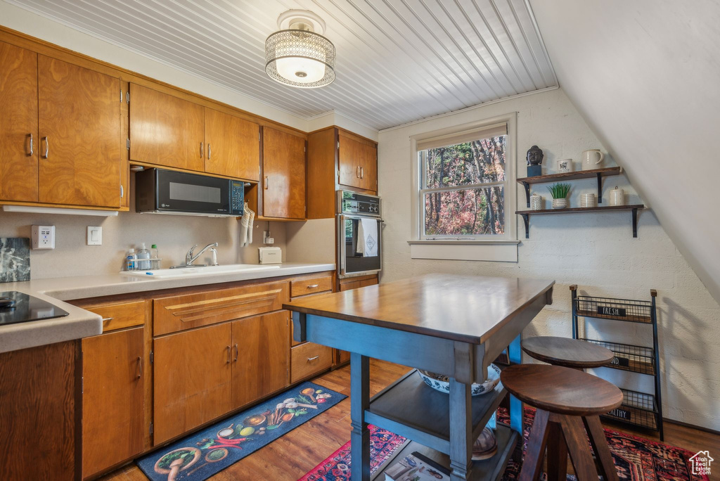 Kitchen with hardwood / wood-style flooring, wooden ceiling, ornamental molding, black appliances, and sink