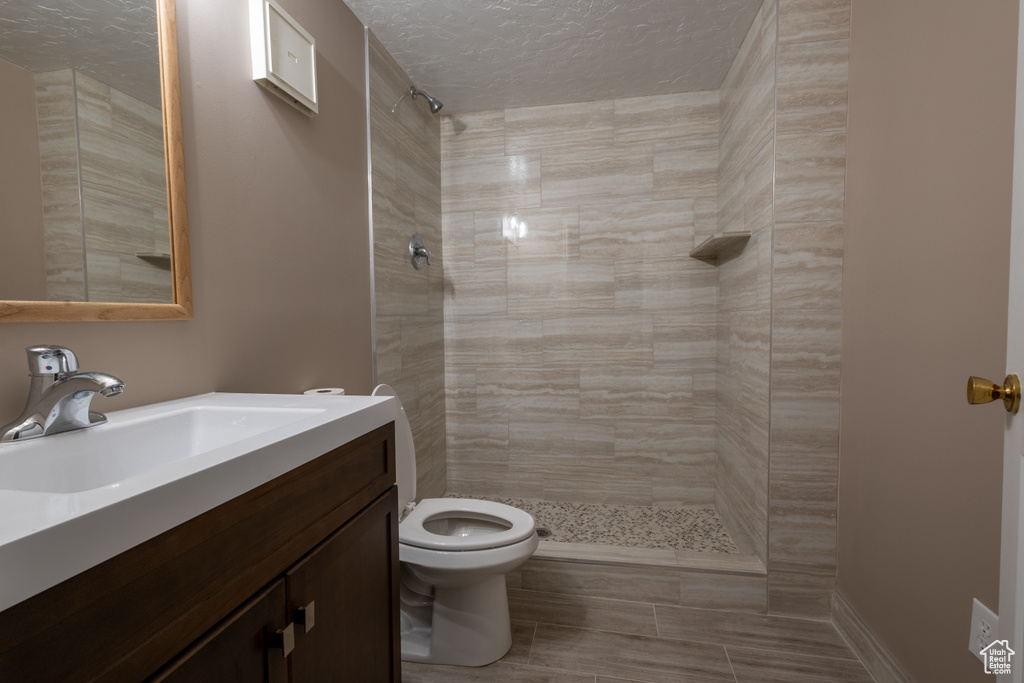 Bathroom with vanity, tiled shower, a textured ceiling, and toilet