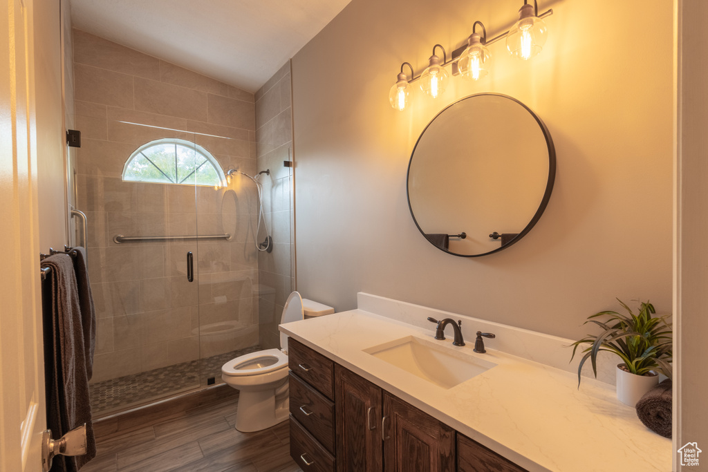 Bathroom with lofted ceiling, a shower with door, wood-type flooring, toilet, and vanity