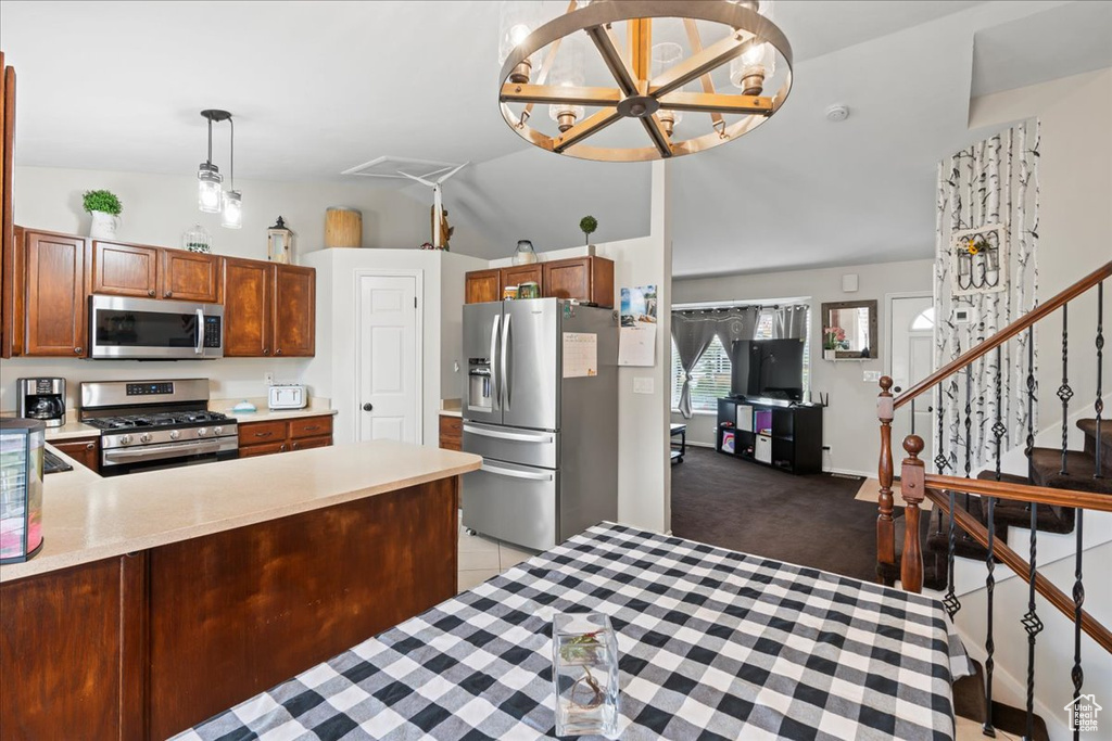 Kitchen featuring lofted ceiling, kitchen peninsula, a notable chandelier, light colored carpet, and appliances with stainless steel finishes