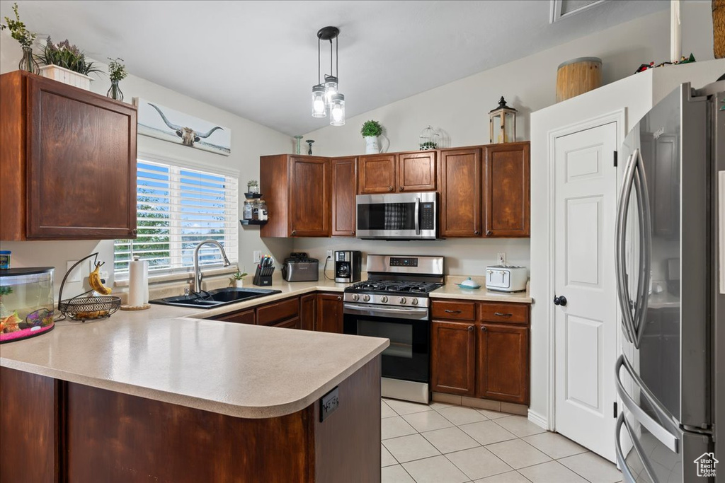 Kitchen with kitchen peninsula, hanging light fixtures, appliances with stainless steel finishes, vaulted ceiling, and sink