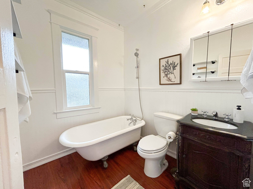 Bathroom with wood-type flooring, a bath, toilet, vanity, and ornamental molding