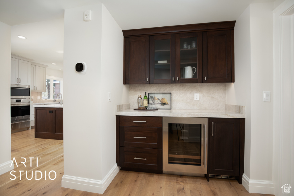 Bar featuring light hardwood / wood-style flooring, double oven, dark brown cabinets, and backsplash