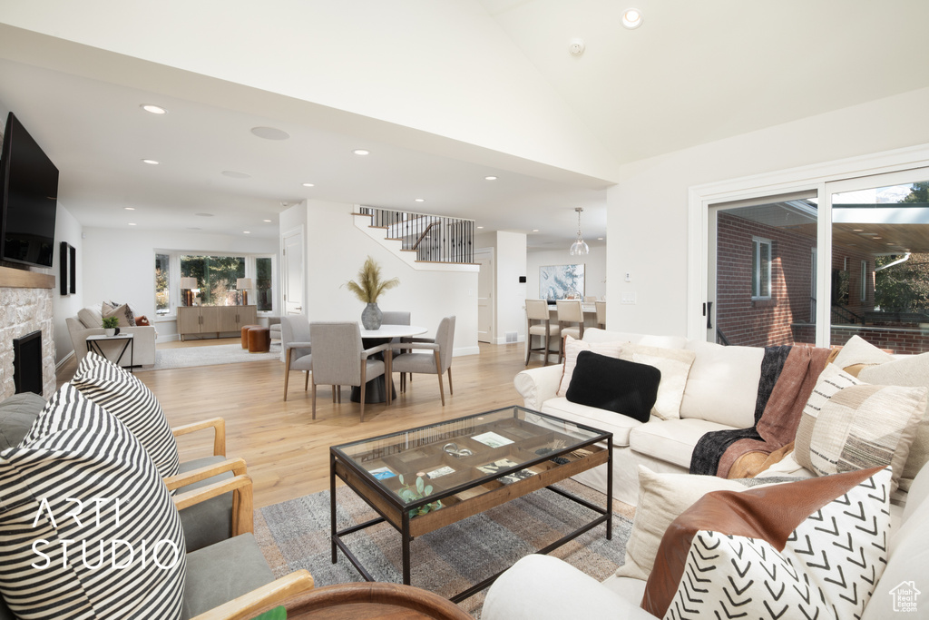 Living room featuring a stone fireplace, vaulted ceiling, and light wood-type flooring