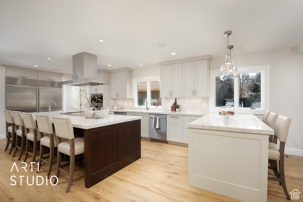 Kitchen featuring appliances with stainless steel finishes, white cabinetry, a center island, island range hood, and decorative light fixtures