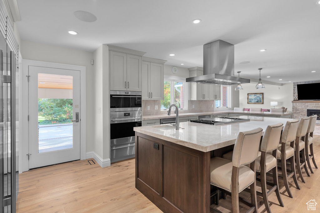 Kitchen featuring island exhaust hood, light hardwood / wood-style flooring, an island with sink, and stainless steel double oven