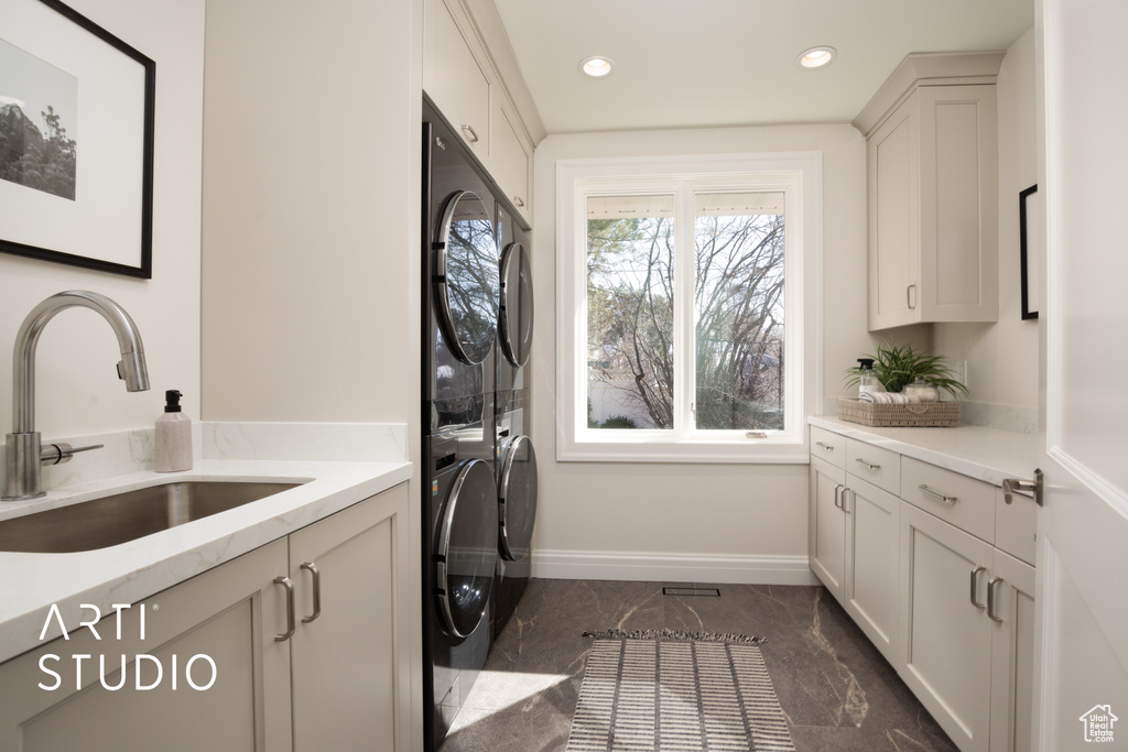 Clothes washing area featuring cabinets, stacked washer and dryer, and sink