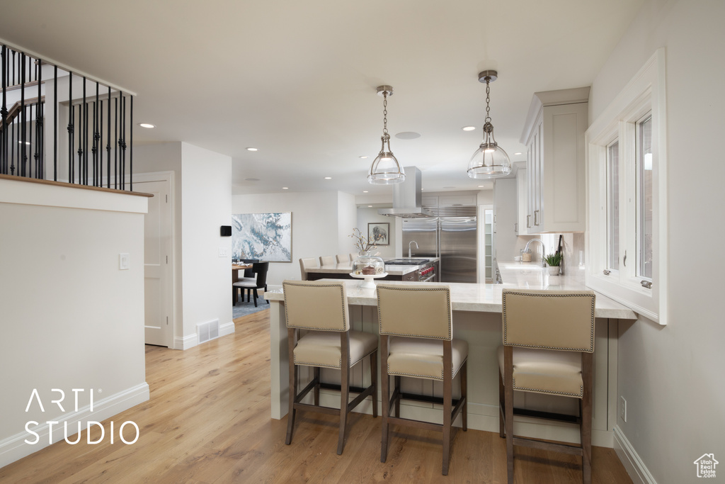 Kitchen featuring white cabinets, a kitchen breakfast bar, built in refrigerator, light hardwood / wood-style floors, and kitchen peninsula