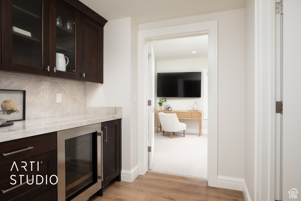 Bar featuring wine cooler, backsplash, light stone counters, dark brown cabinets, and light wood-type flooring