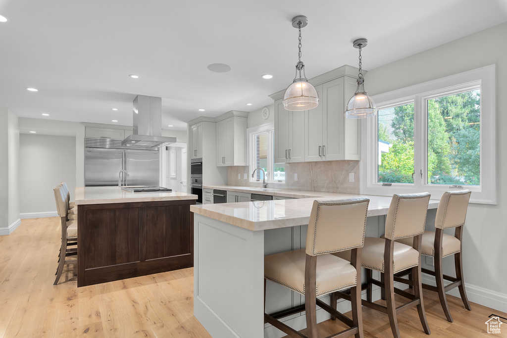 Kitchen featuring island range hood, a kitchen island, decorative light fixtures, and light hardwood / wood-style floors